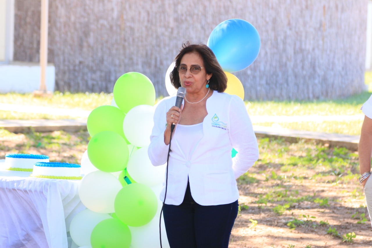 Una funcionaria con micrófono habla durante el acto de aniversario, junto a una decoración de globos verdes y blancos