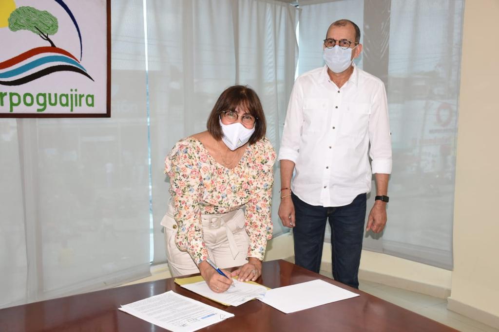 Una mujer firma la resolución de comisión conjunta sobre una mesa, junto a un hombre de pie, con el logo de Corpoguajira al fondo