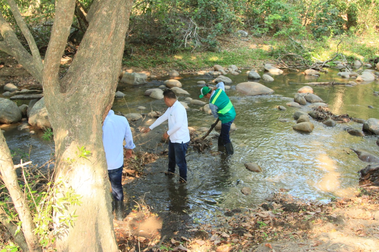 Funcionarios con chaleco verde miden el caudal del río junto a la bocatoma, entre rocas