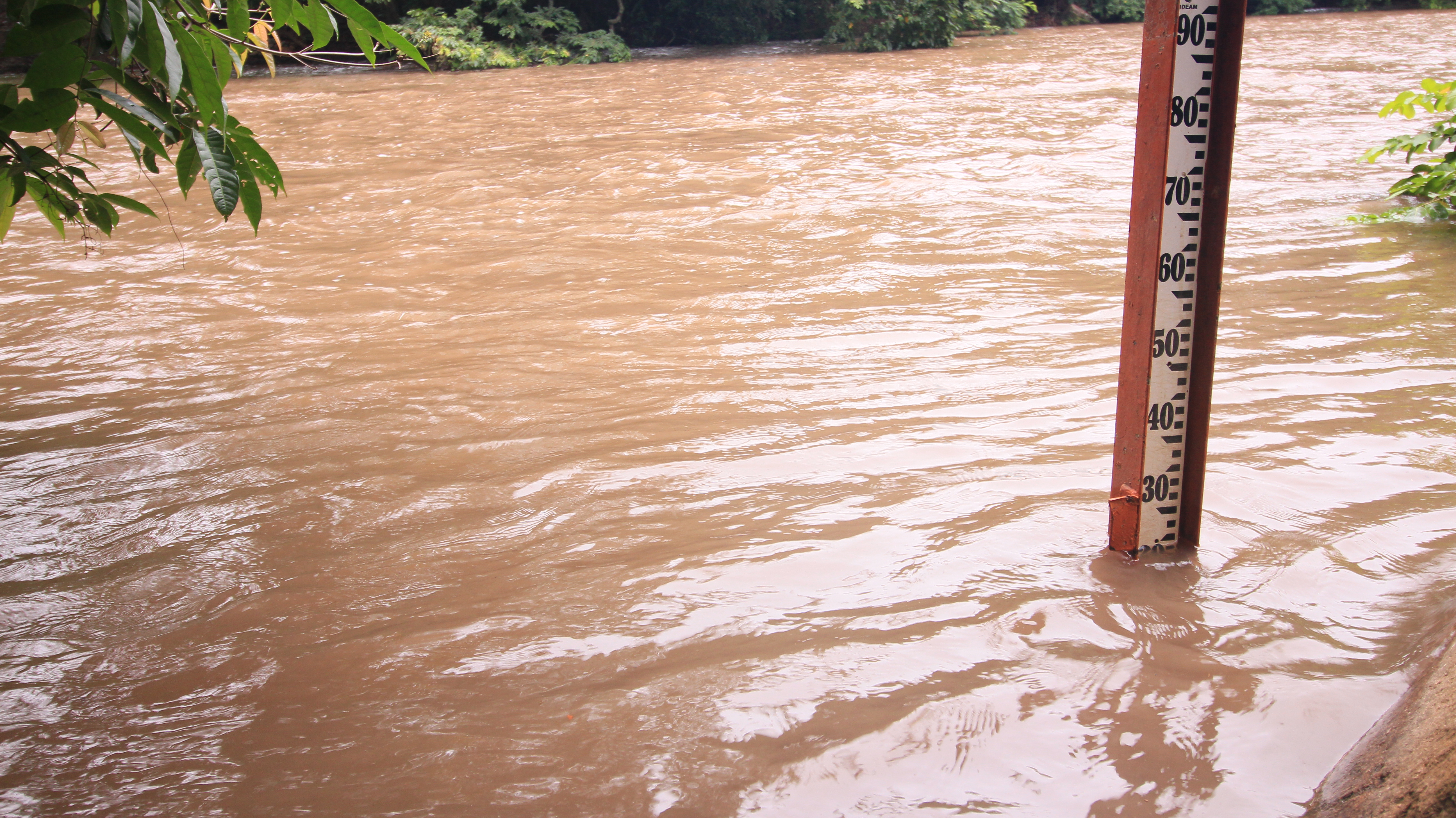 Río crecido de aguas turbias junto a una regla de medición de nivel