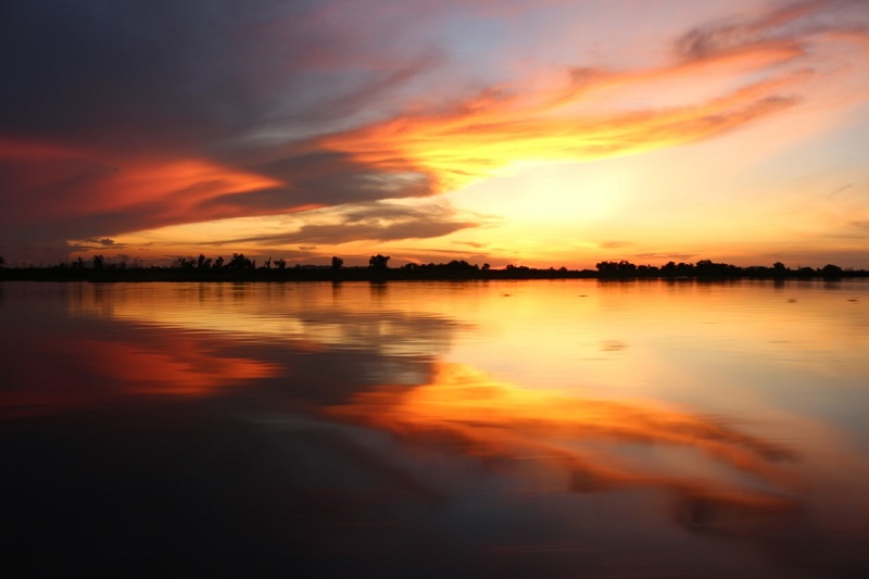 Atardecer sobre el humedal con el cielo naranja reflejado en el agua