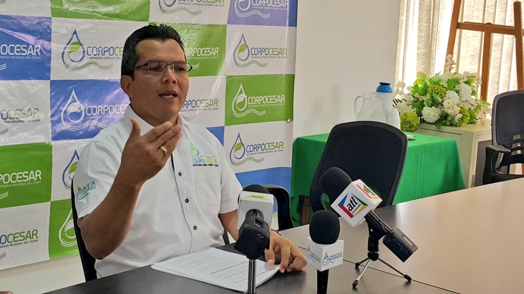 El director de Corpocesar habla en una rueda de prensa frente a un fondo con el logo de Corpocesar, con micrófonos de varios medios sobre la mesa