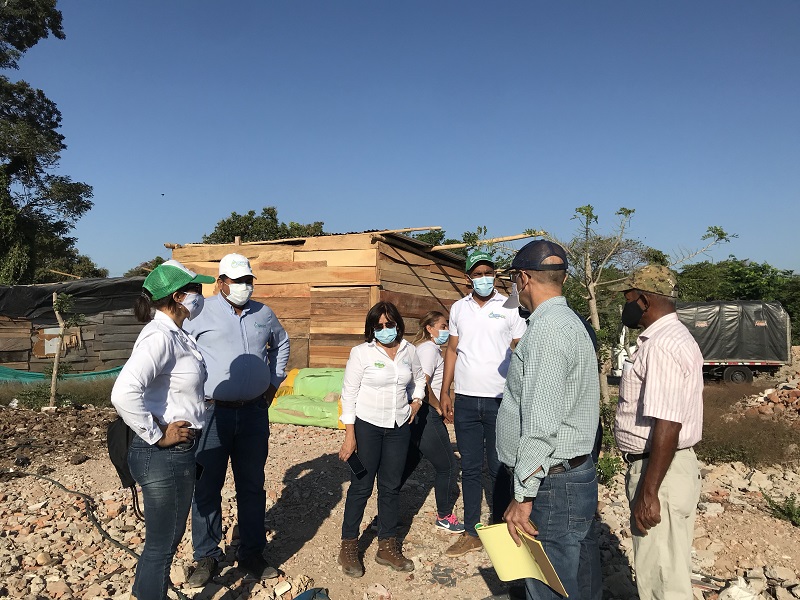 Funcionarios y habitantes conversan frente a una vivienda de madera en un terreno invadido