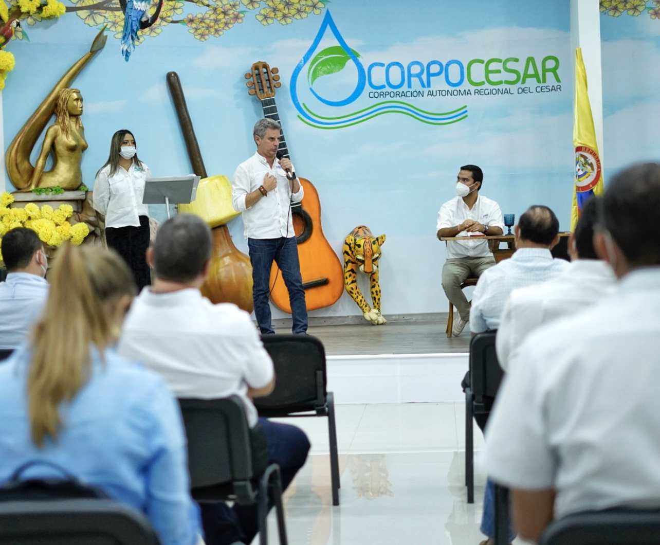 Funcionarios y asistentes sentados en un auditorio con un mural de Corpocesar al fondo durante la jornada de siembra