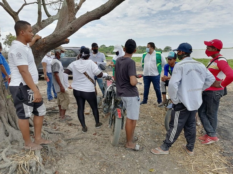 Funcionarios y habitantes conversan en un terreno junto a un árbol grande durante la visita de control
