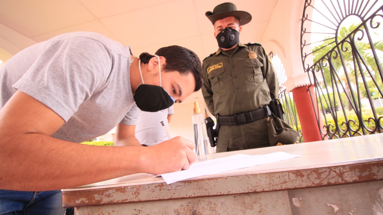 Un hombre con tapabocas firma un documento ante un policía durante la entrega voluntaria