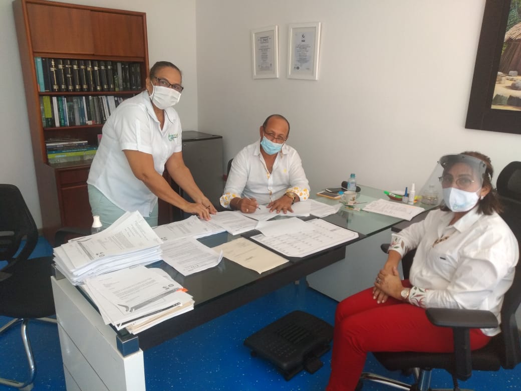 Dos funcionarias y un funcionario con tapabocas revisan documentos sobre un escritorio