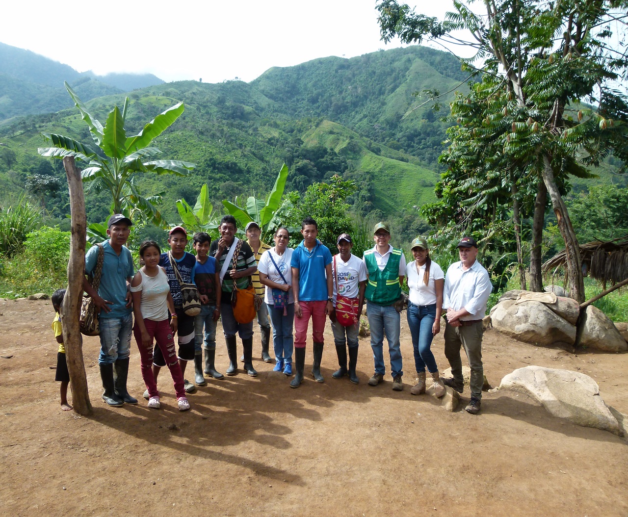 Grupo de personas, con un funcionario de chaleco verde, posa en un camino de tierra con montañas verdes al fondo.