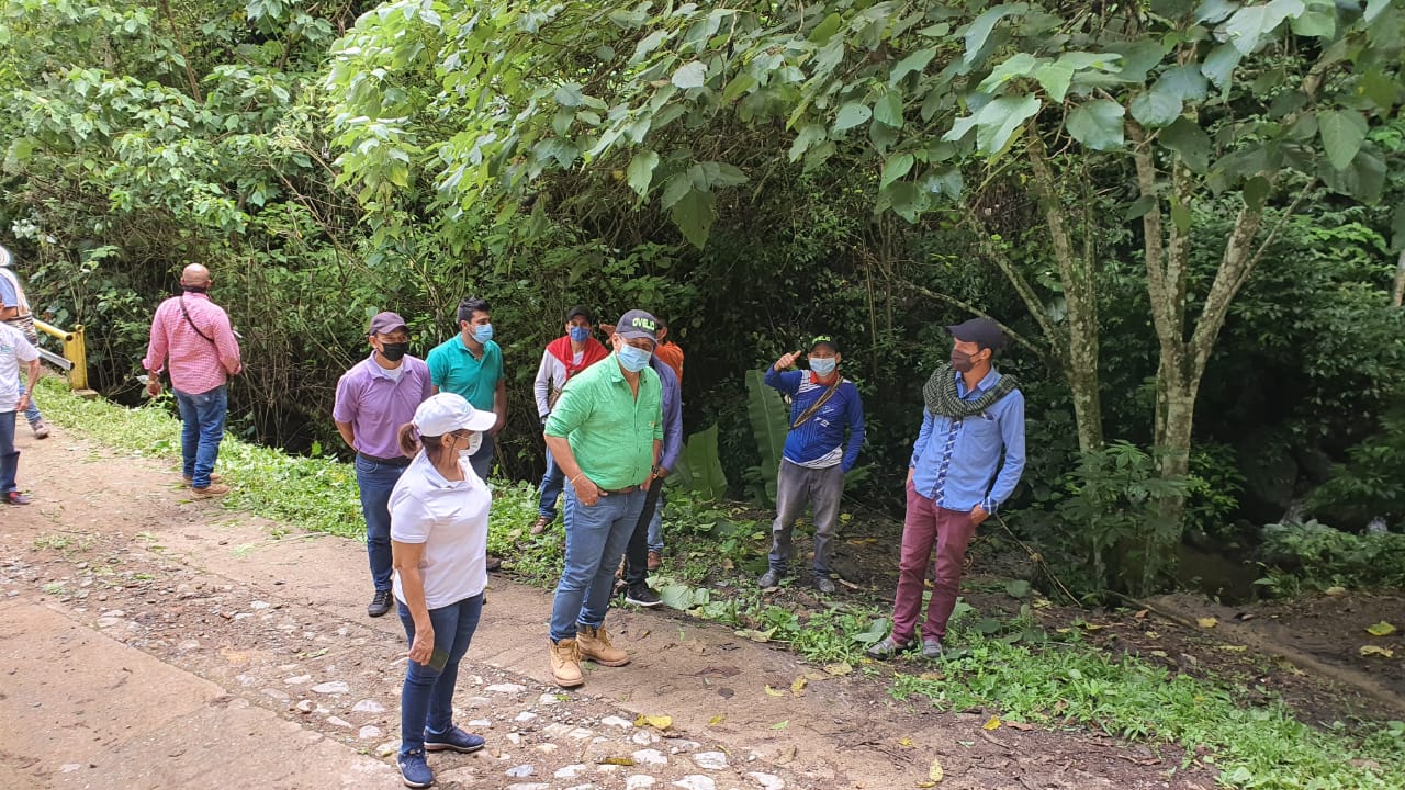Funcionarios y campesinos de pie en un camino rural con vegetación durante la atención de las denuncias