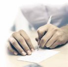 Fotografía de dos manos escribiendo sobre una hoja de papel
