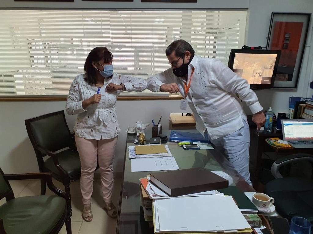 Una funcionaria y un hombre se saludan con los codos en un despacho
